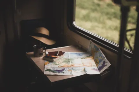 Ilustrasi menyusun itinerary perjalanan liburan dengan peta digital dan catatan rencana perjalanan di kafe