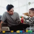 Seorang ayah sedang bermain bersama anak di ruang tamu rumah untuk membangun kedekatan emosional