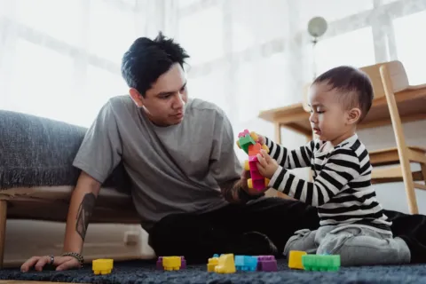 Seorang ayah sedang bermain bersama anak di ruang tamu rumah untuk membangun kedekatan emosional