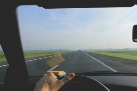 Seseorang sedang memegang setir mobil di jalan tol untuk tips berkendara jarak jauh yang aman