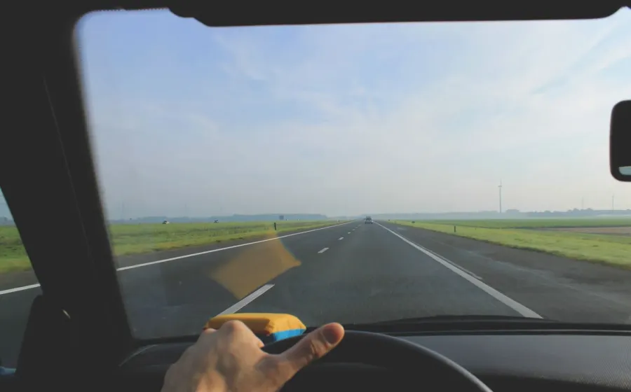 Seseorang sedang memegang setir mobil di jalan tol untuk tips berkendara jarak jauh yang aman
