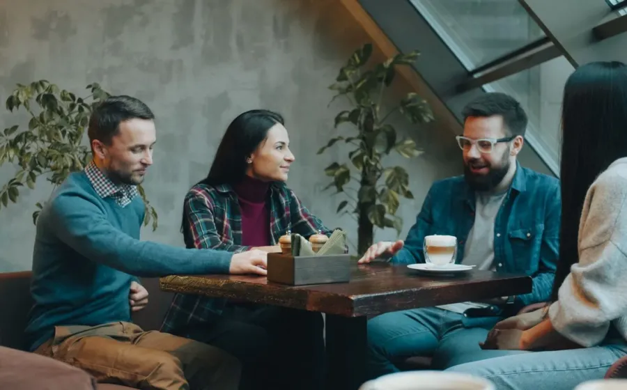 Dua orang sedang mengobrol santai di kedai kopi menerapkan tips bersosialisasi bagi introvert