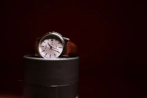 Seseorang memakai jam tangan kasual bertali kulit cokelat yang serasi dengan kemeja rapi.