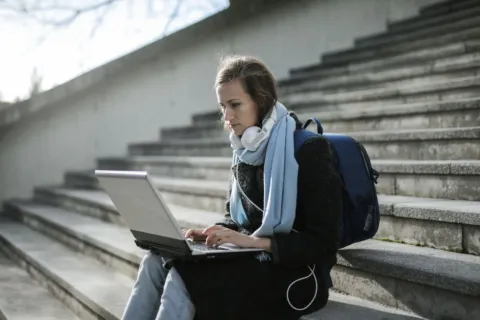 Mahasiswa sedang mengetik tugas kuliah menggunakan laptop fungsional di perpustakaan kampus