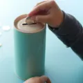 Anak kecil memasukkan uang koin ke dalam celengan transparan untuk belajar menabung