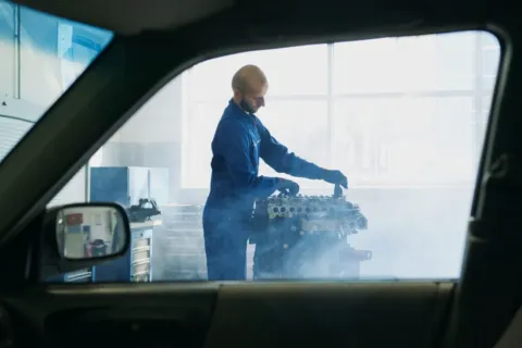 Pengemudi mengecek kap mesin mobil overheat yang mengeluarkan uap di tepi jalan